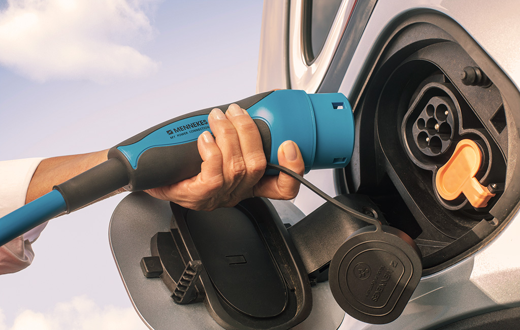 Nahaufnahme einer Hand, die ein MENNEKES-Ladekabel an ein Elektroauto anschließt
